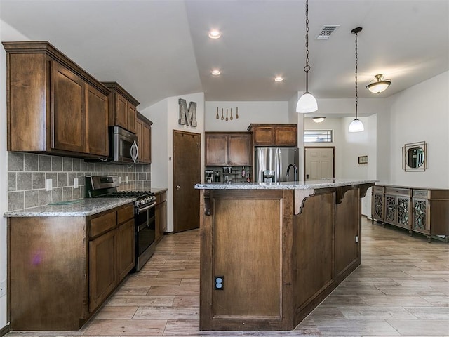 kitchen featuring visible vents, a breakfast bar, stainless steel appliances, light wood-type flooring, and backsplash