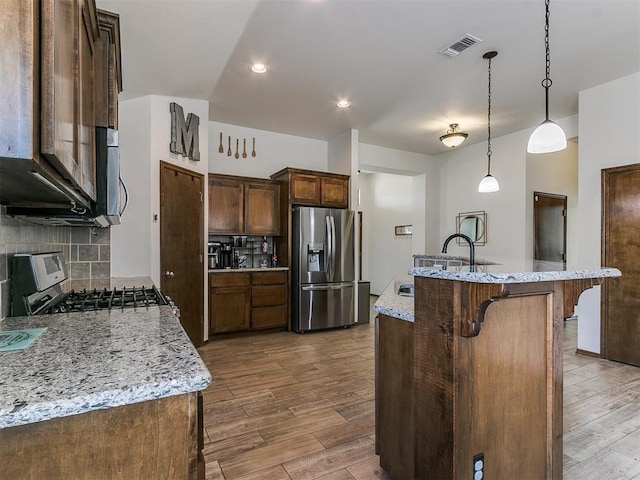 kitchen featuring visible vents, a sink, backsplash, wood finished floors, and stainless steel appliances