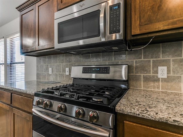 kitchen featuring backsplash, dark brown cabinetry, light stone counters, and appliances with stainless steel finishes