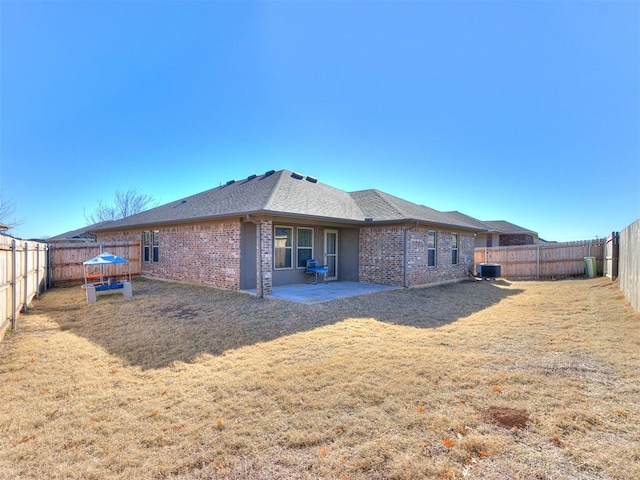 rear view of house with central AC, a fenced backyard, a yard, brick siding, and a patio area