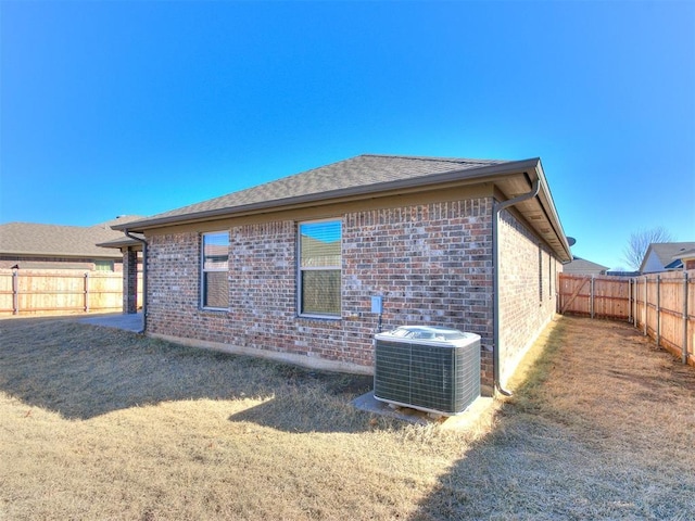 back of house with central air condition unit, a fenced backyard, and brick siding