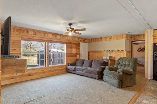 carpeted living room featuring ceiling fan and wood walls
