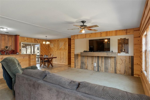 carpeted living area with wooden walls and ceiling fan with notable chandelier