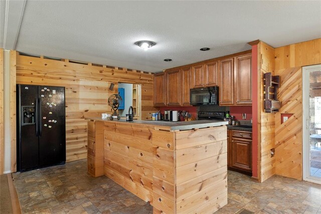 kitchen with wooden walls, black appliances, a center island, and stone finish floor