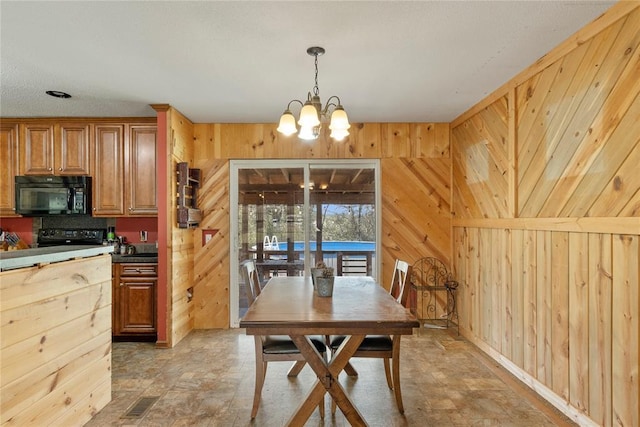 dining area featuring wooden walls, a chandelier, and stone finish floor