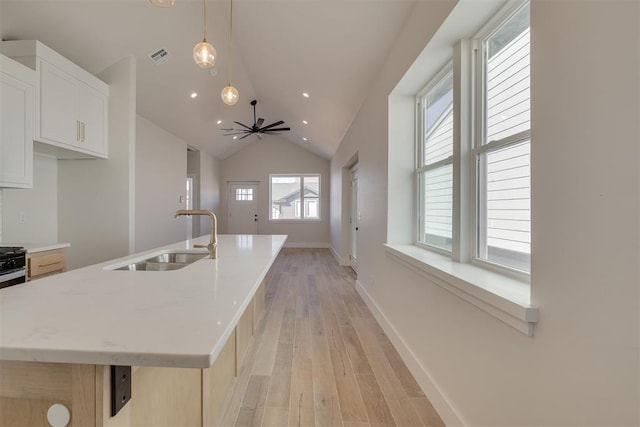 kitchen featuring visible vents, an island with sink, a sink, vaulted ceiling, and light wood-style floors