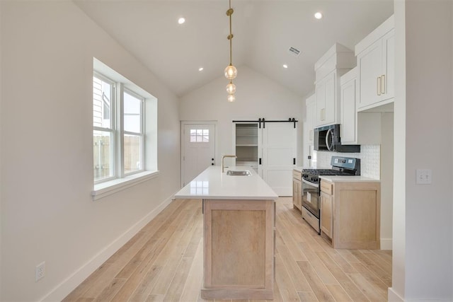 kitchen with visible vents, a sink, appliances with stainless steel finishes, a barn door, and light wood-type flooring