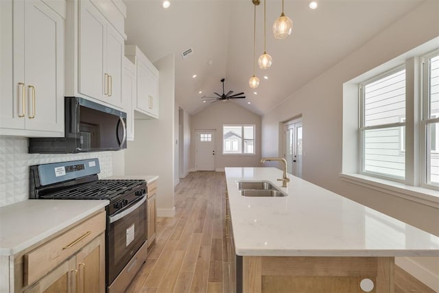 kitchen with a center island with sink, a sink, tasteful backsplash, light wood finished floors, and stainless steel gas range