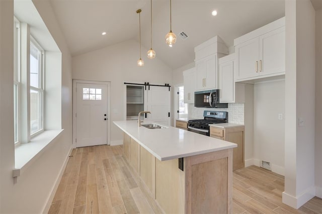 kitchen featuring visible vents, black microwave, light wood-style flooring, stainless steel gas stove, and a sink