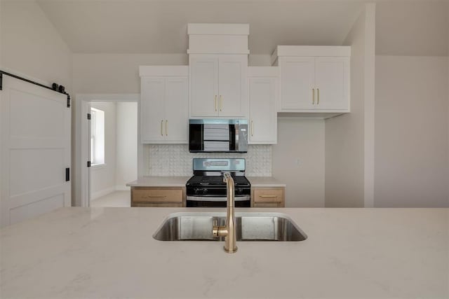 kitchen featuring a sink, decorative backsplash, appliances with stainless steel finishes, white cabinetry, and a barn door