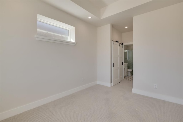 spare room featuring light carpet, recessed lighting, baseboards, and a barn door