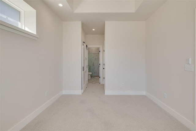 spare room with a barn door, recessed lighting, light carpet, and baseboards