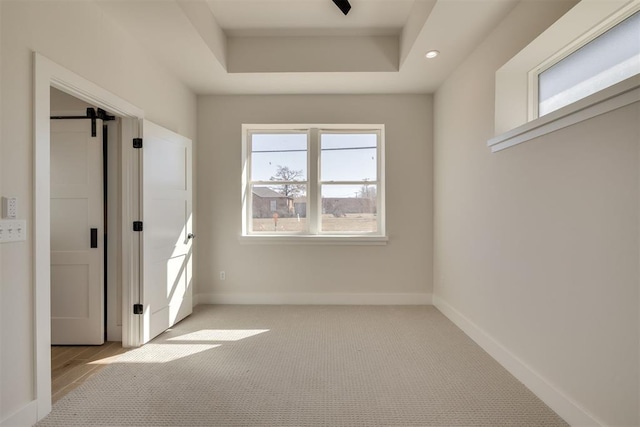 interior space with baseboards, a barn door, light carpet, recessed lighting, and a raised ceiling