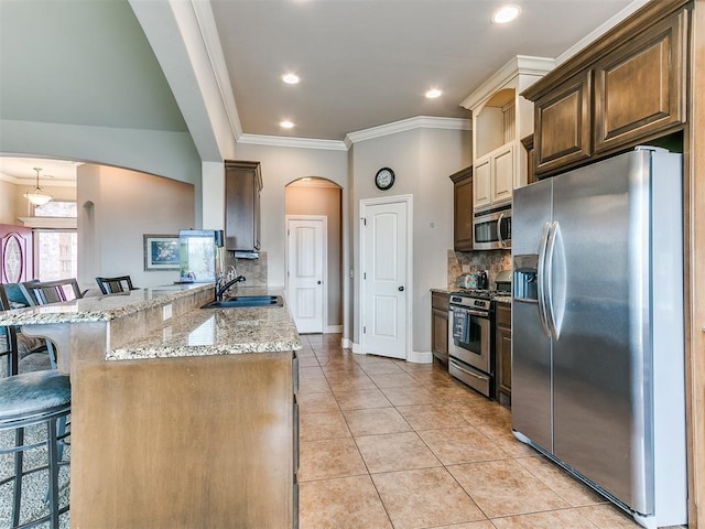 kitchen featuring a kitchen bar, a sink, arched walkways, appliances with stainless steel finishes, and light tile patterned flooring