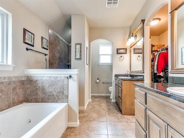 bathroom with visible vents, a bathing tub, two vanities, a sink, and toilet