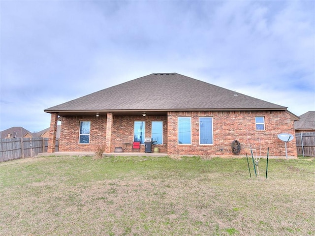 back of house with brick siding, roof with shingles, a yard, and fence