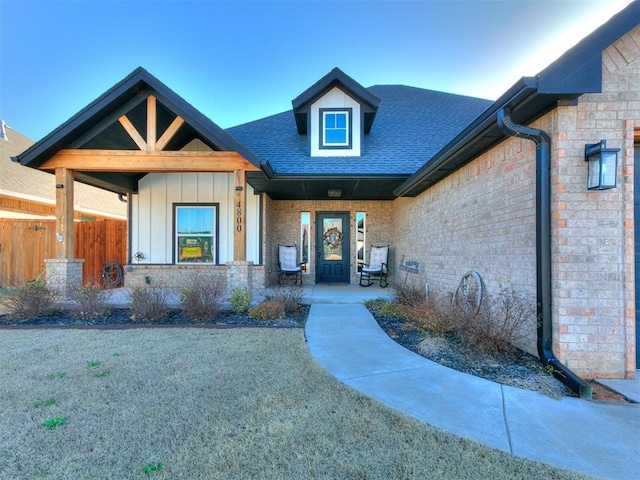 view of front of property with fence, roof with shingles, covered porch, board and batten siding, and brick siding