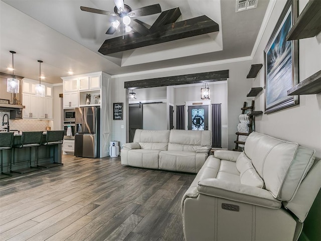 living room featuring dark wood-style floors, a ceiling fan, visible vents, a tray ceiling, and ornamental molding