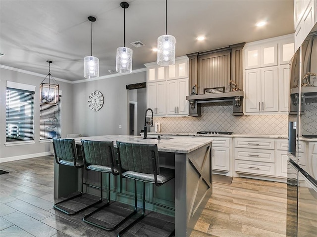 kitchen featuring a sink, a center island with sink, crown molding, and light wood finished floors