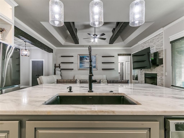 kitchen with a raised ceiling, a sink, open floor plan, freestanding refrigerator, and light stone countertops