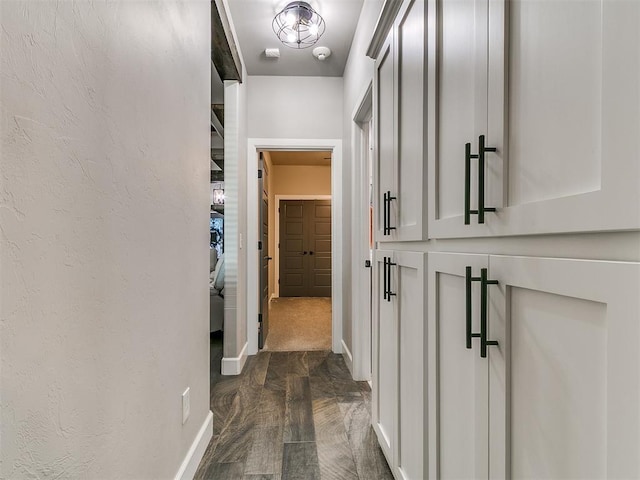 hall featuring a textured wall and baseboards