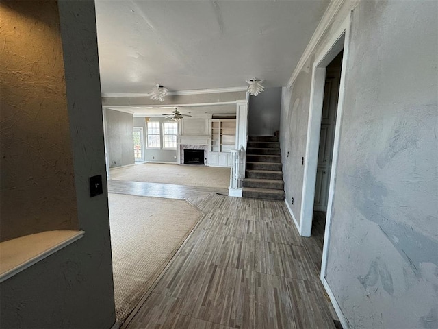 unfurnished living room featuring crown molding, a premium fireplace, ceiling fan, stairs, and a textured wall