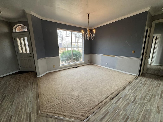 unfurnished dining area featuring wainscoting, baseboards, crown molding, and an inviting chandelier