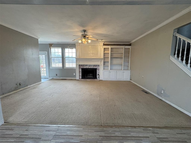 unfurnished living room with a high end fireplace, visible vents, ornamental molding, carpet flooring, and a ceiling fan