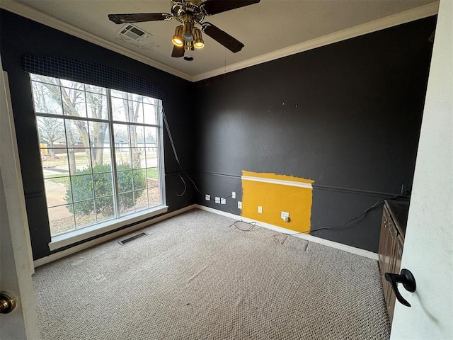 carpeted spare room with a ceiling fan, crown molding, baseboards, and visible vents