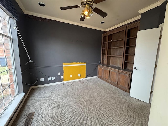 empty room with crown molding, visible vents, carpet floors, and ceiling fan