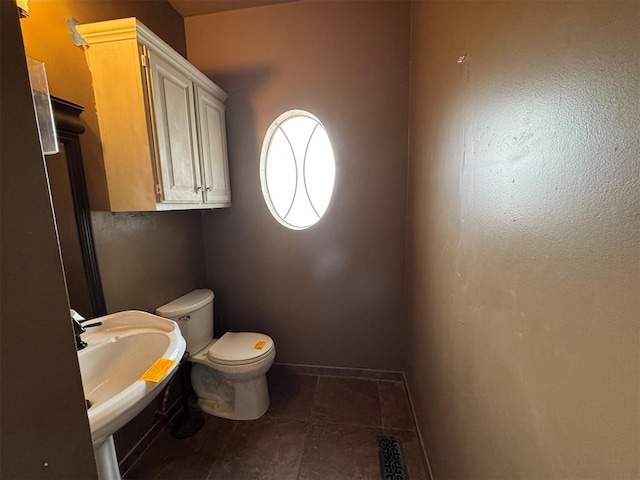 half bath featuring toilet, baseboards, visible vents, and a sink