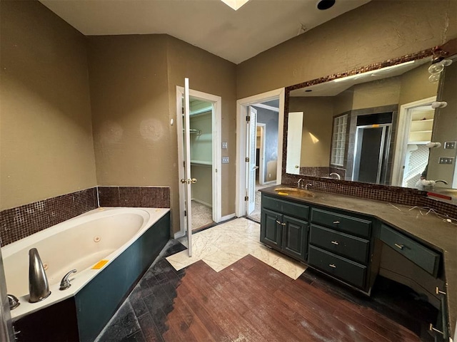 full bathroom with a walk in closet, a stall shower, a jetted tub, wood finished floors, and vanity