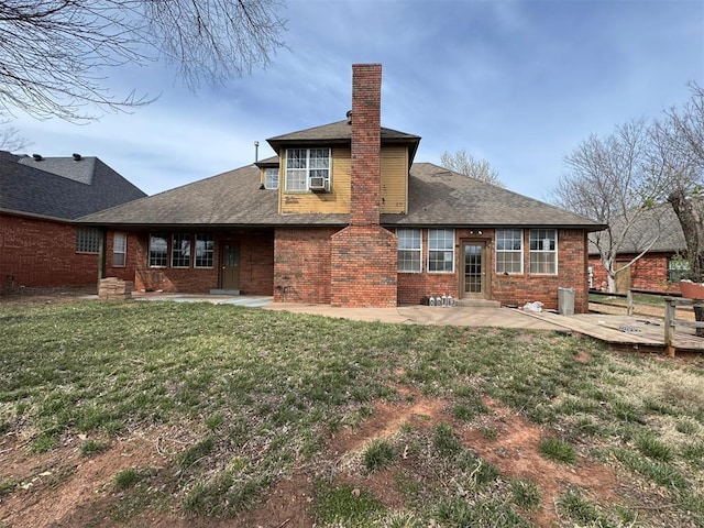 rear view of house with brick siding, roof with shingles, a lawn, a chimney, and a patio area