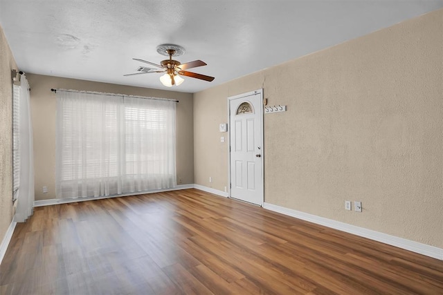 unfurnished room featuring a textured wall, baseboards, ceiling fan, and wood finished floors