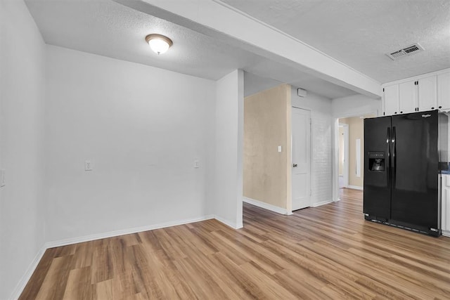 empty room with light wood-style flooring, baseboards, visible vents, and a textured ceiling