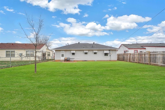 back of property with a fenced backyard, a shingled roof, and a yard