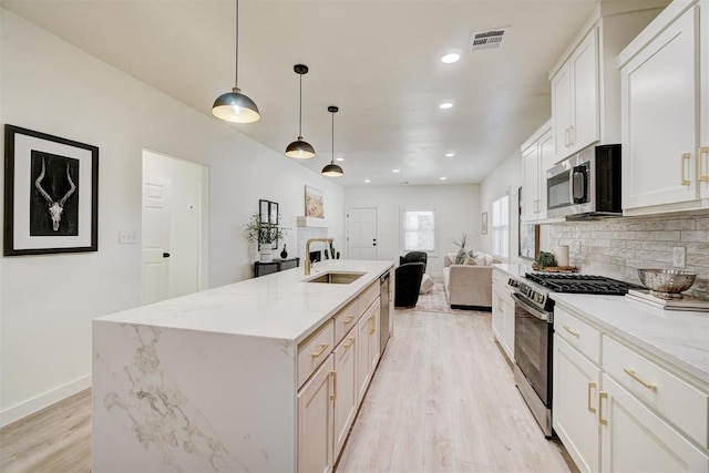 kitchen with visible vents, light wood finished floors, a sink, decorative backsplash, and stainless steel appliances