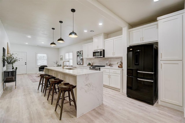 kitchen with a kitchen island with sink, a sink, stainless steel appliances, white cabinetry, and tasteful backsplash