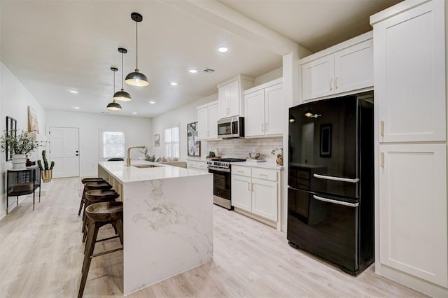 kitchen featuring light wood-type flooring, a kitchen island with sink, backsplash, stainless steel appliances, and white cabinets