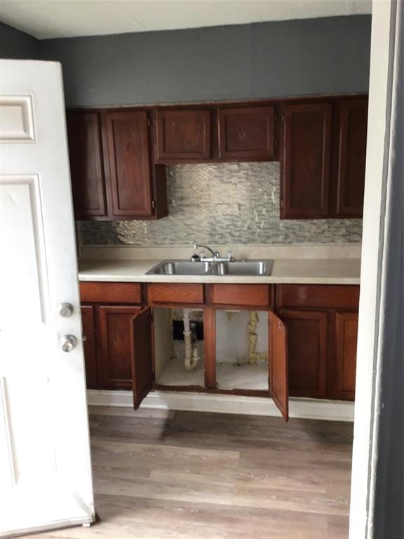 kitchen featuring a sink, decorative backsplash, light wood-style floors, and light countertops