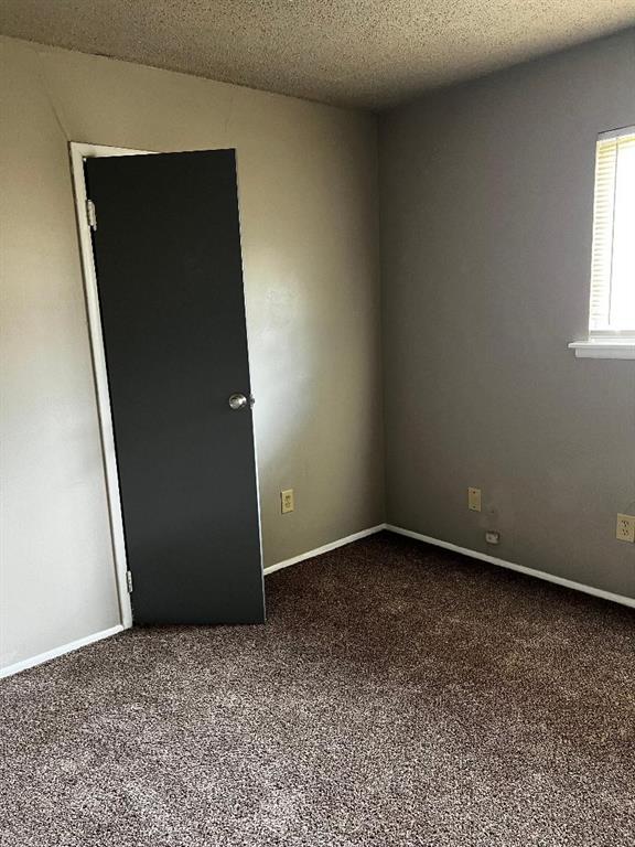 2513 N Nottingham Way, Moore, OK 73160 - empty room with dark carpet, a textured ceiling, and baseboards