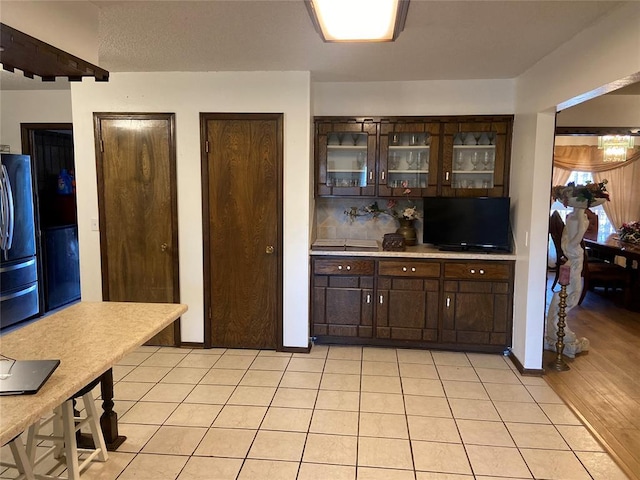 2416 SW 92nd St, Oklahoma City, OK 73159 - kitchen with tasteful backsplash, dark brown cabinetry, glass insert cabinets, light tile patterned floors, and freestanding refrigerator