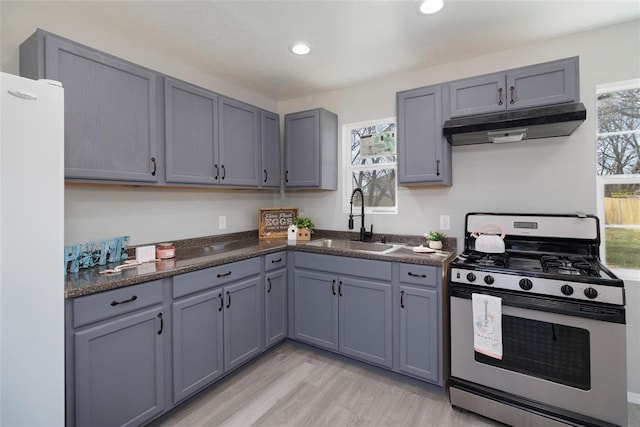 kitchen with a sink, freestanding refrigerator, under cabinet range hood, gas stove, and dark countertops