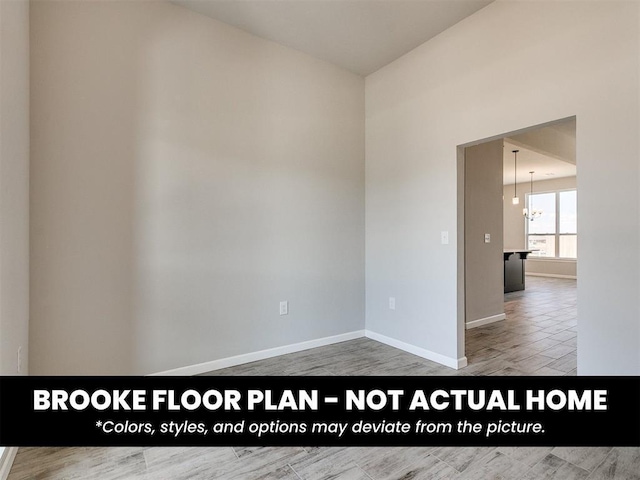 spare room with baseboards, wood finished floors, and an inviting chandelier