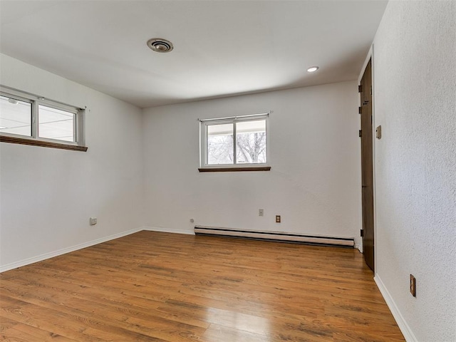 empty room with visible vents, wood finished floors, baseboards, and a baseboard radiator