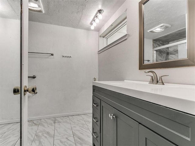 bathroom with baseboards, vanity, marble finish floor, a textured ceiling, and a shower