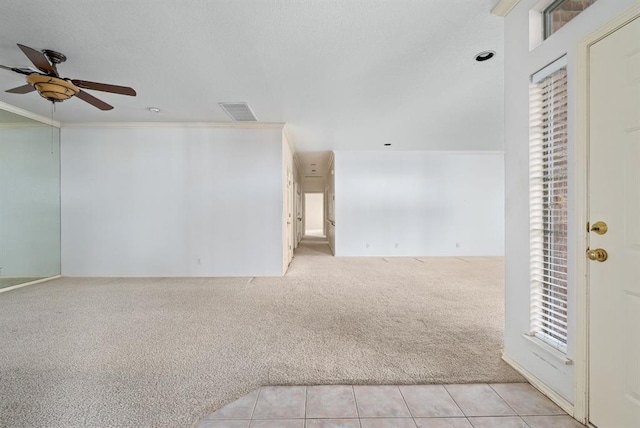 empty room with visible vents, light carpet, ornamental molding, a ceiling fan, and light tile patterned flooring
