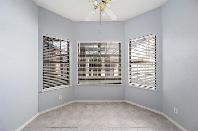 tiled empty room featuring baseboards and ceiling fan