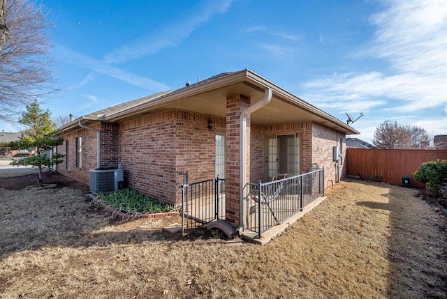 view of property exterior featuring brick siding, central air condition unit, and fence
