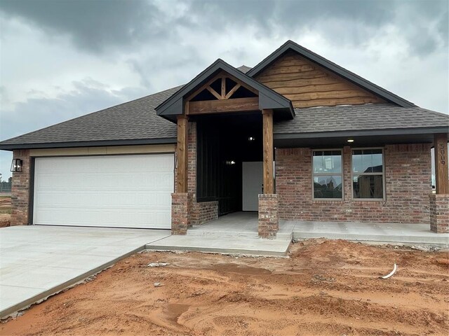 view of front of home with an attached garage, roof with shingles, brick siding, and concrete driveway